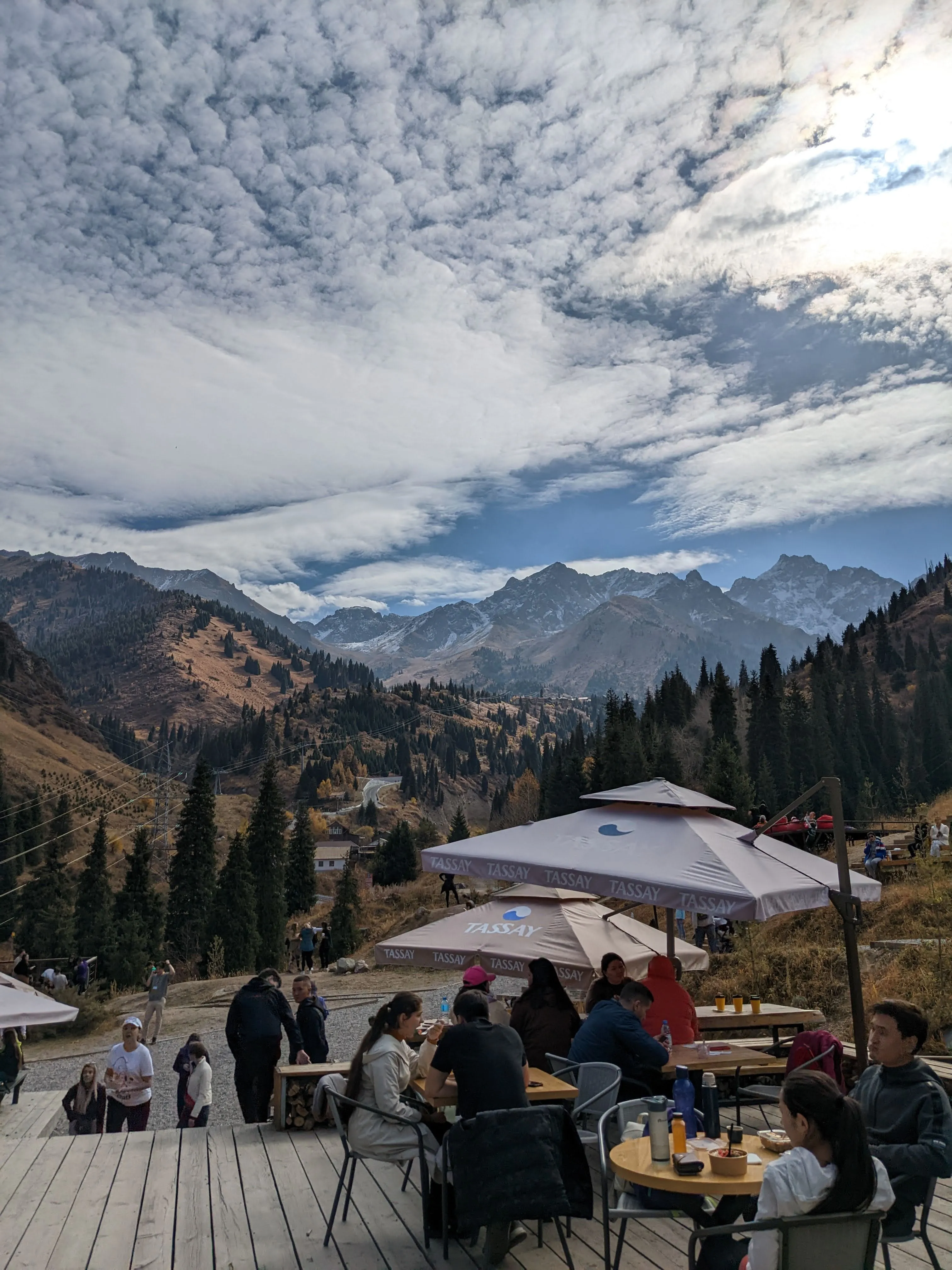 The terrace at Apa Katya above Gorelnik: wooden decking, full tables under parasols, and snow-dusted peaks across the valley