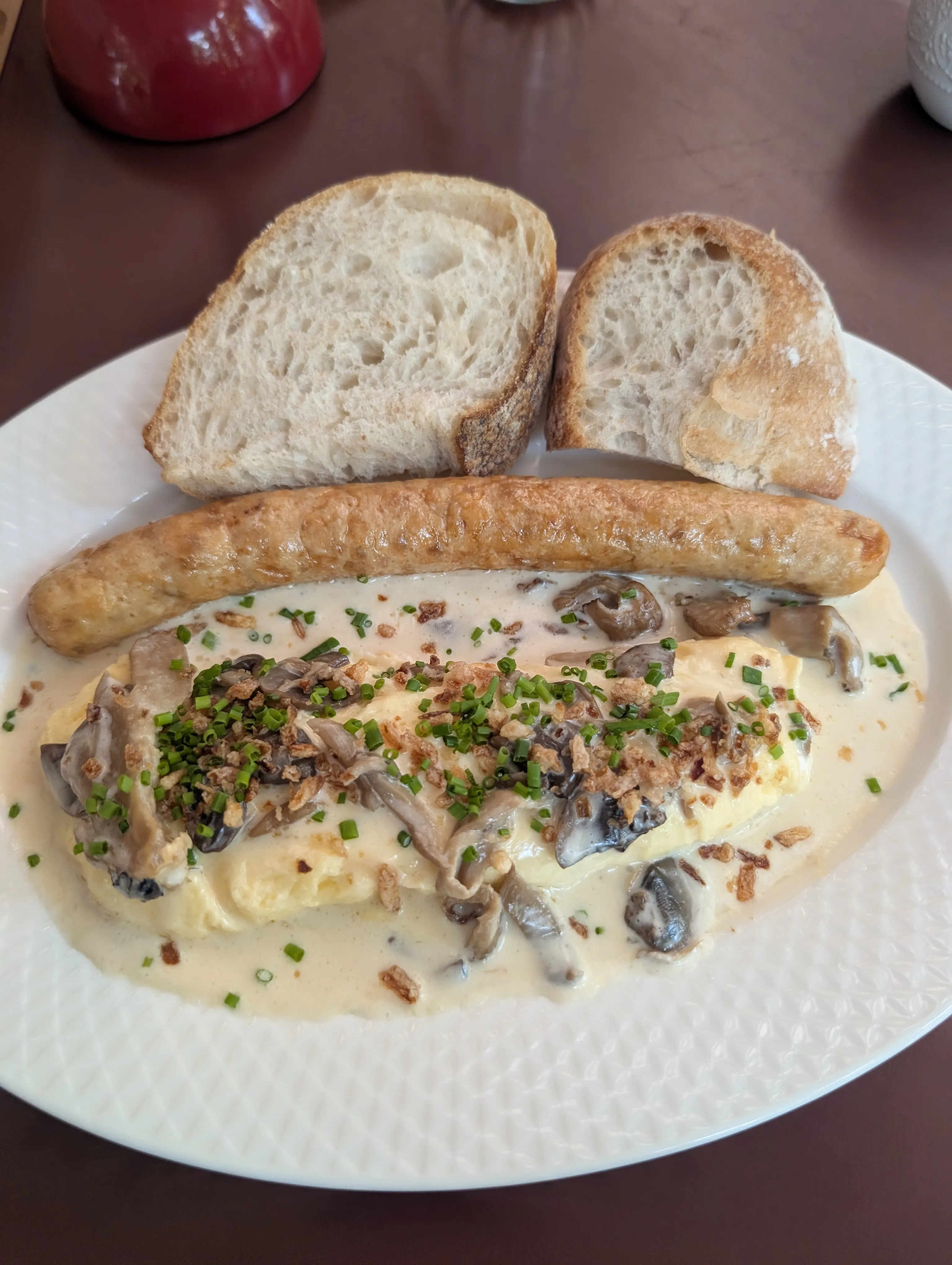 An omelette with mushroom sauce, a chicken sausage and bread on a white plate at Bal