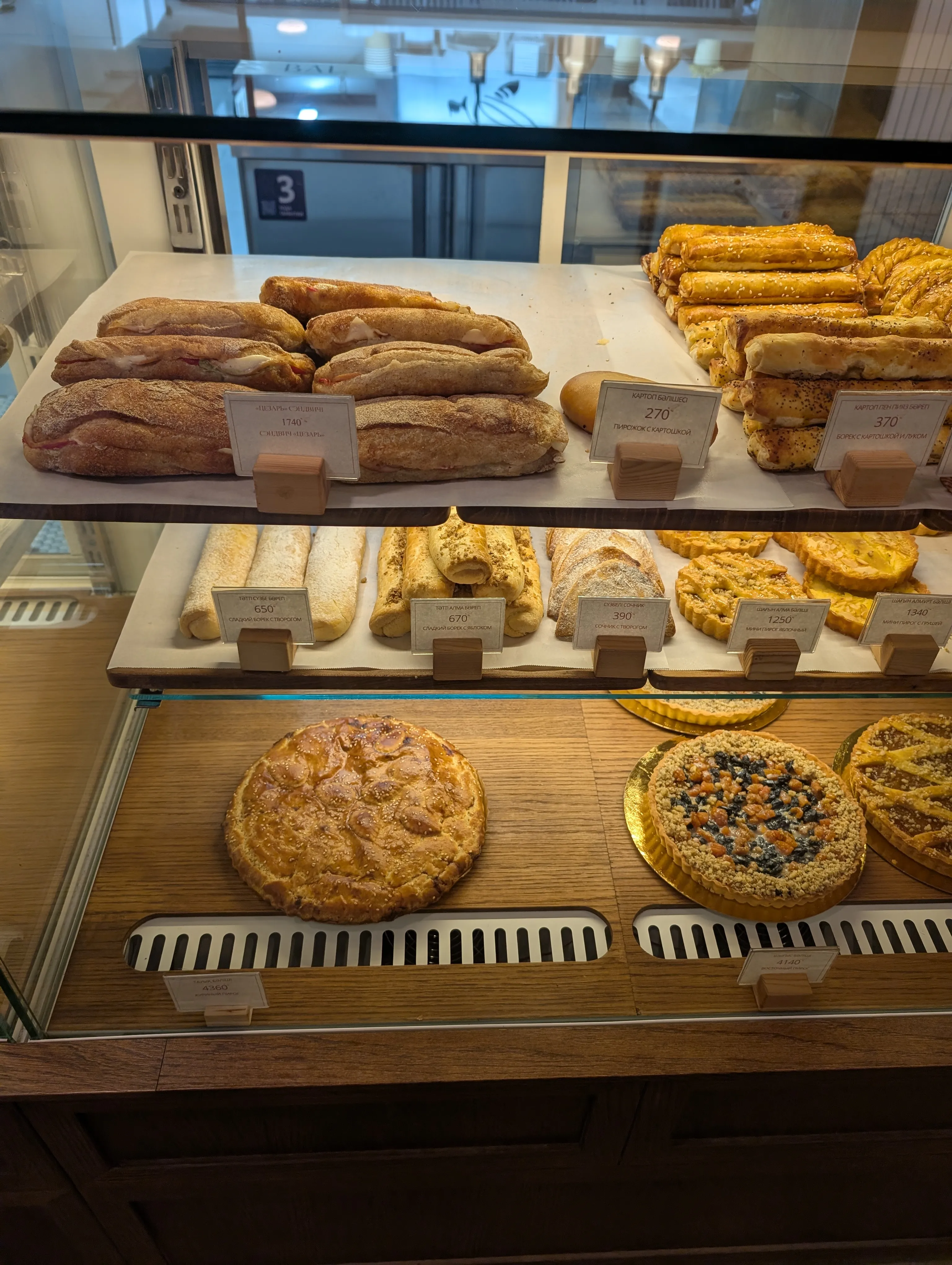 The bakery case at Bal: bureks, pirozhki and pies with handwritten price cards in Kazakh and Russian
