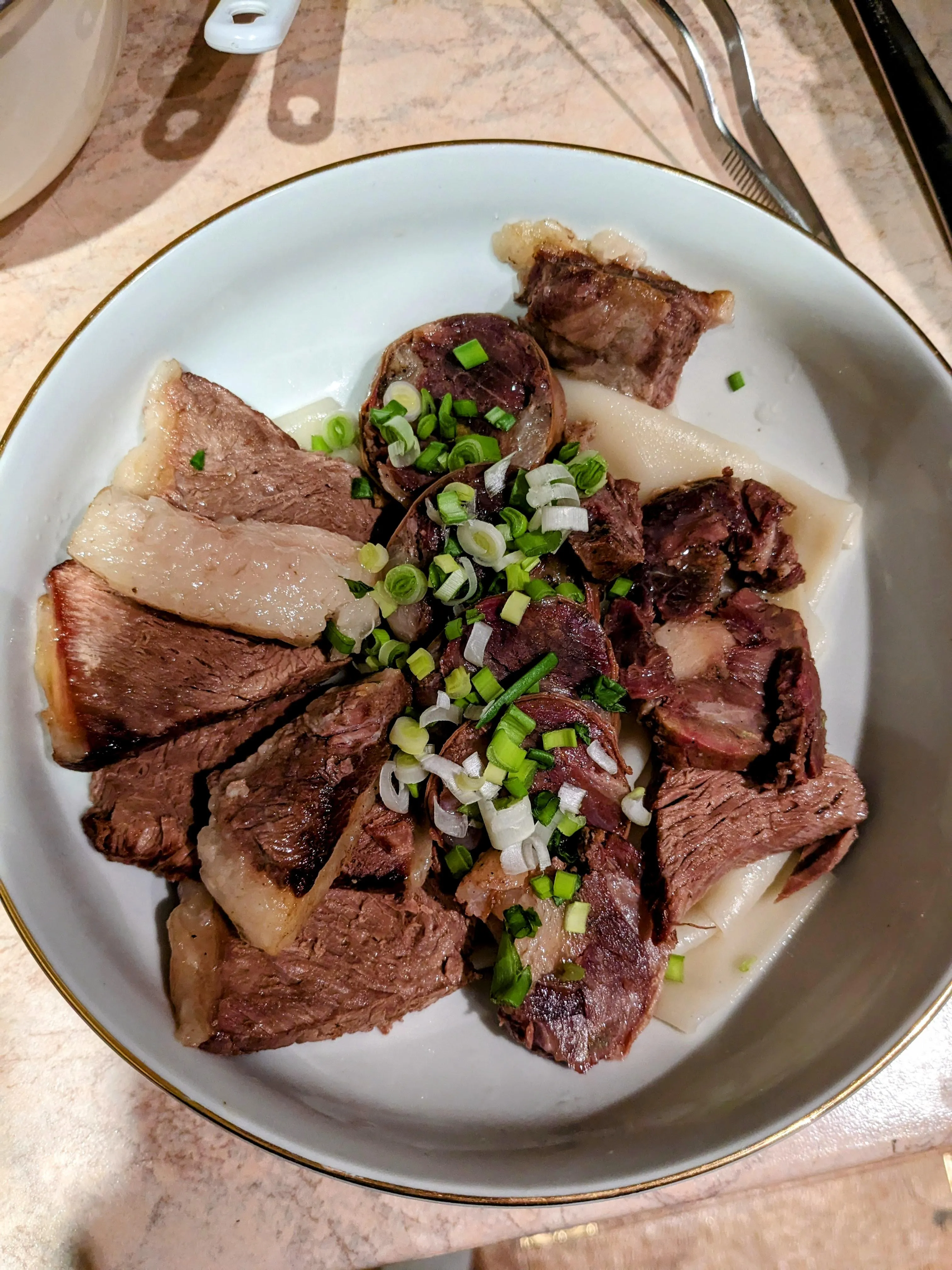 Beshbarmak cooked at home: sliced boiled meat and rounds of kazy fanned over the noodle sheets