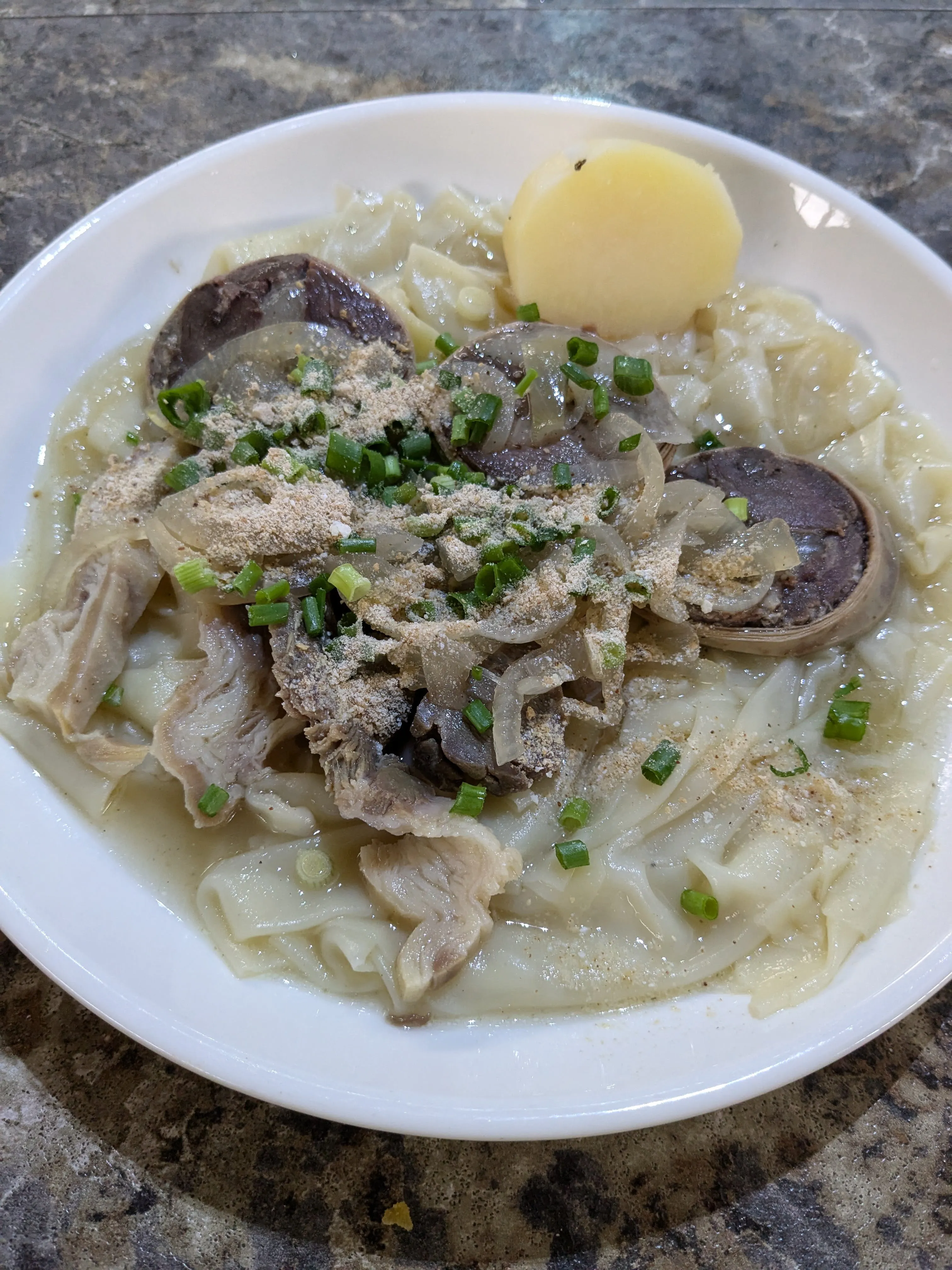 A bowl of beshbarmak at the Green Bazaar: flat noodles in broth under boiled meat and rounds of kazy