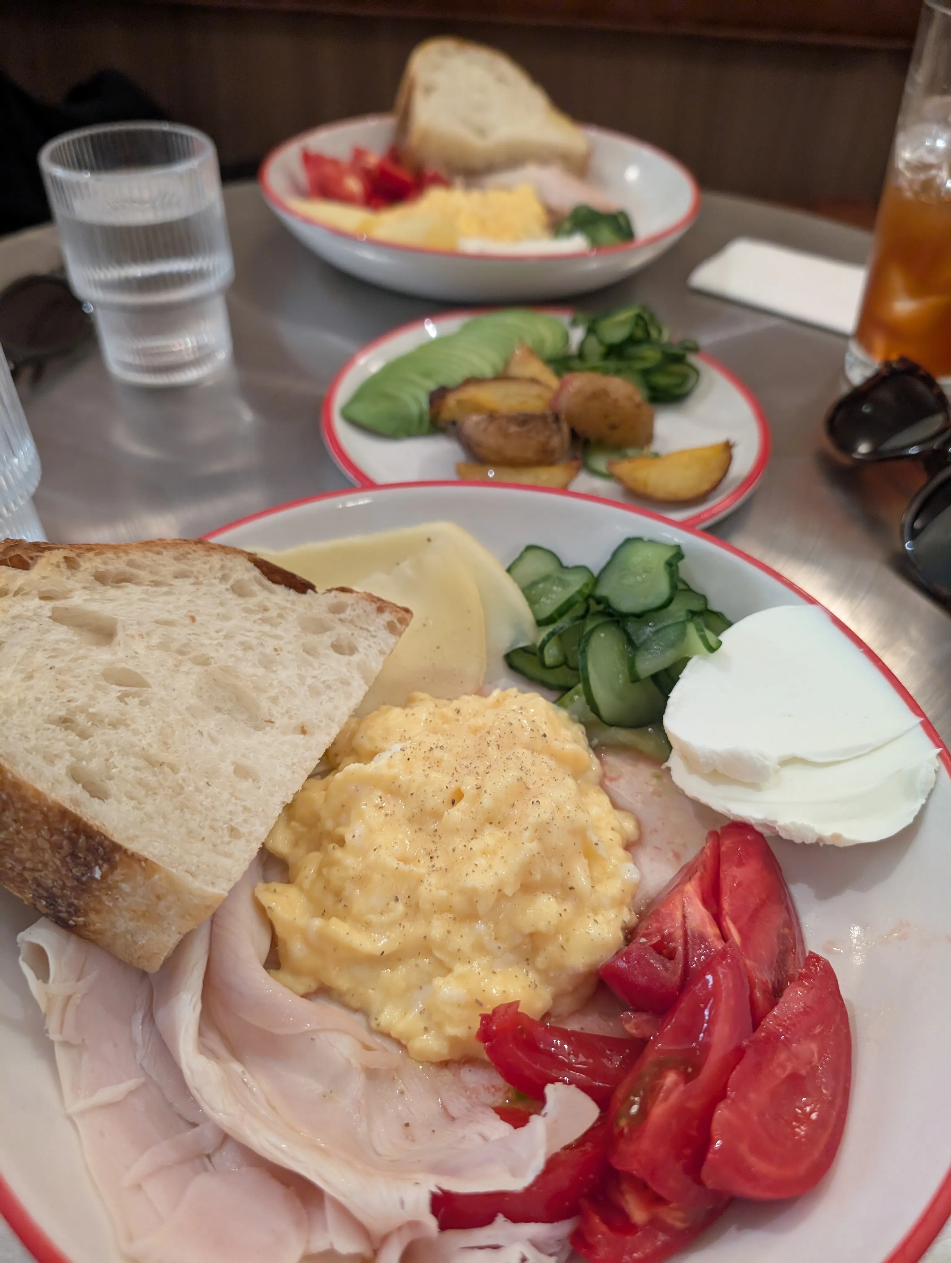 Breakfast at Voronka: scrambled eggs, ham, cheese, sourdough, tomato and cucumber on a rimmed plate, with an iced tea