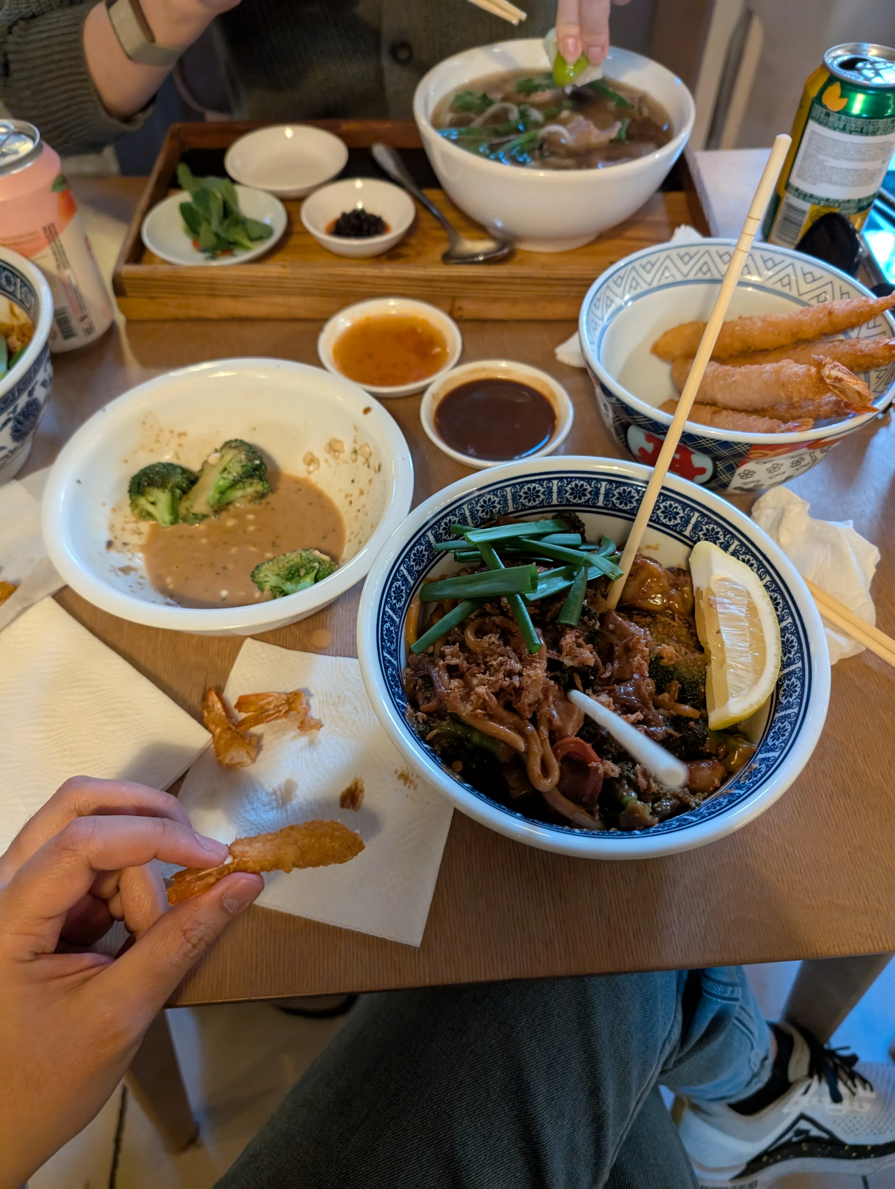 A table at Cece: a blue-and-white bowl of thick wok noodles with beef, broccoli and spring onion under a lemon wedge, a bowl of tempura prawns beside it and small dishes of dipping sauce