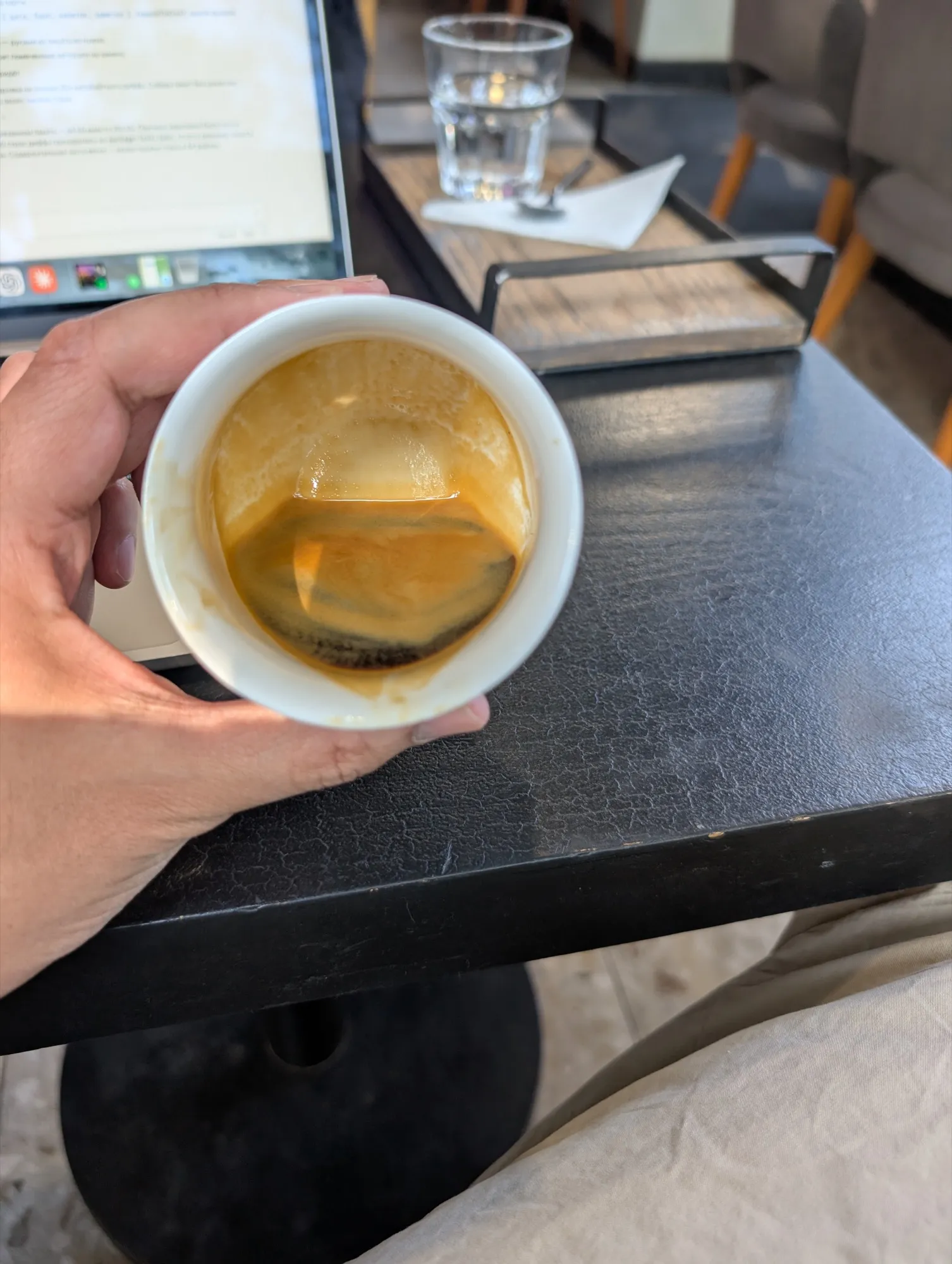 An espresso at Do.Star held up over the table, the crema broken across the surface, with an open laptop and a glass of water on a wooden tray behind it