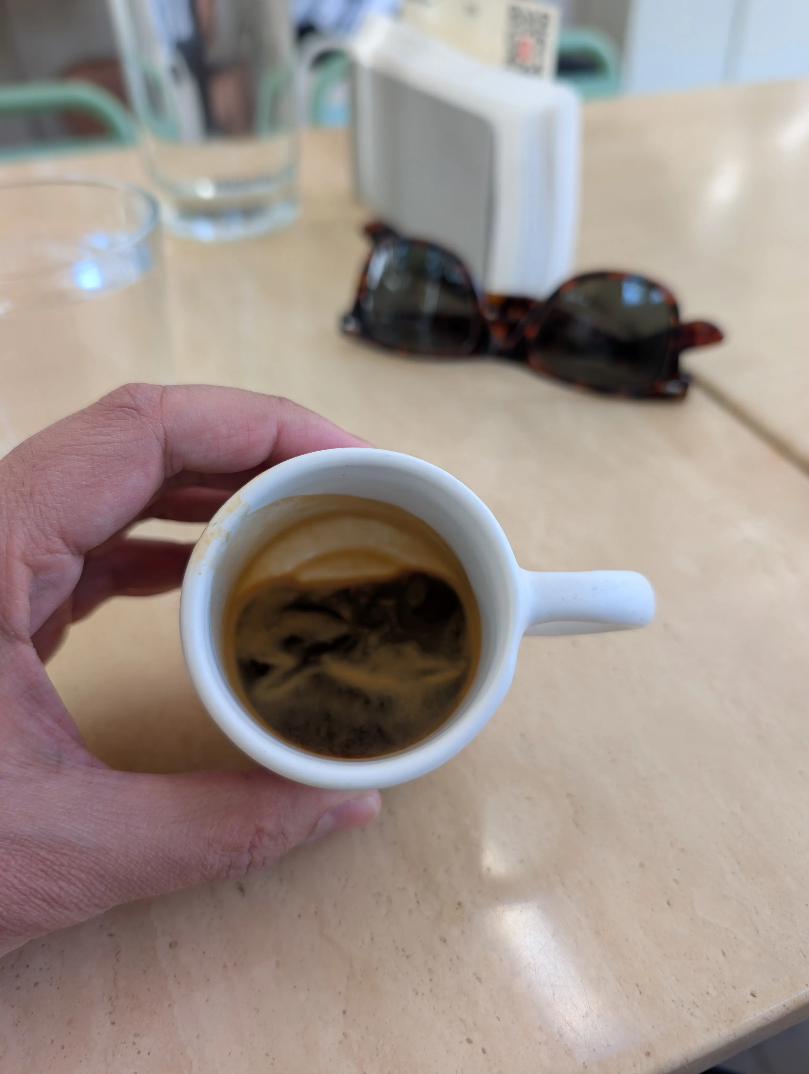 An espresso in a small white cup, held over a stone table at Six Bogenbay