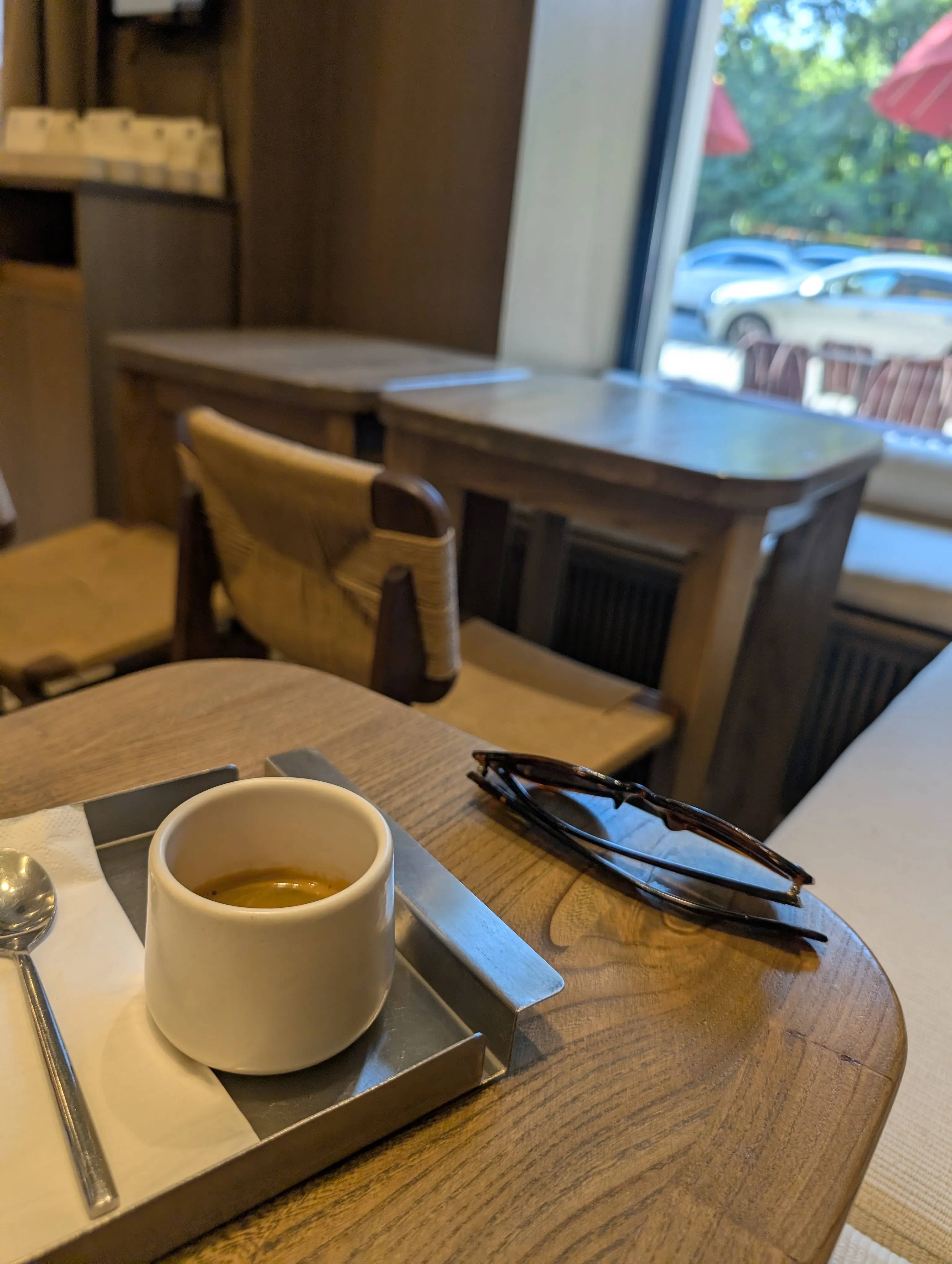 An espresso at Julius on Kabanbai Batyr, in a white cup on a steel tray, on a wooden table by the window with the terrace parasols outside