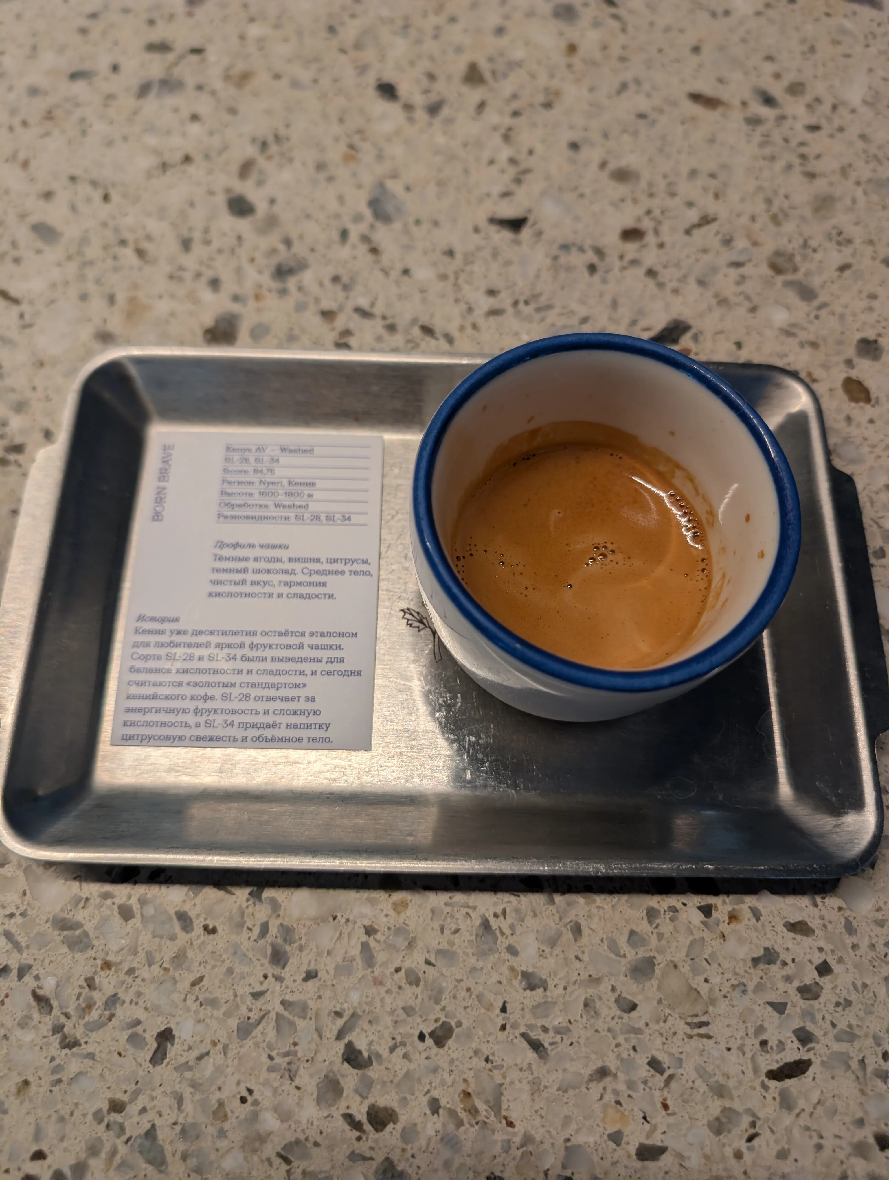 An espresso at Fika on a steel tray beside its bean card, on a terrazzo table
