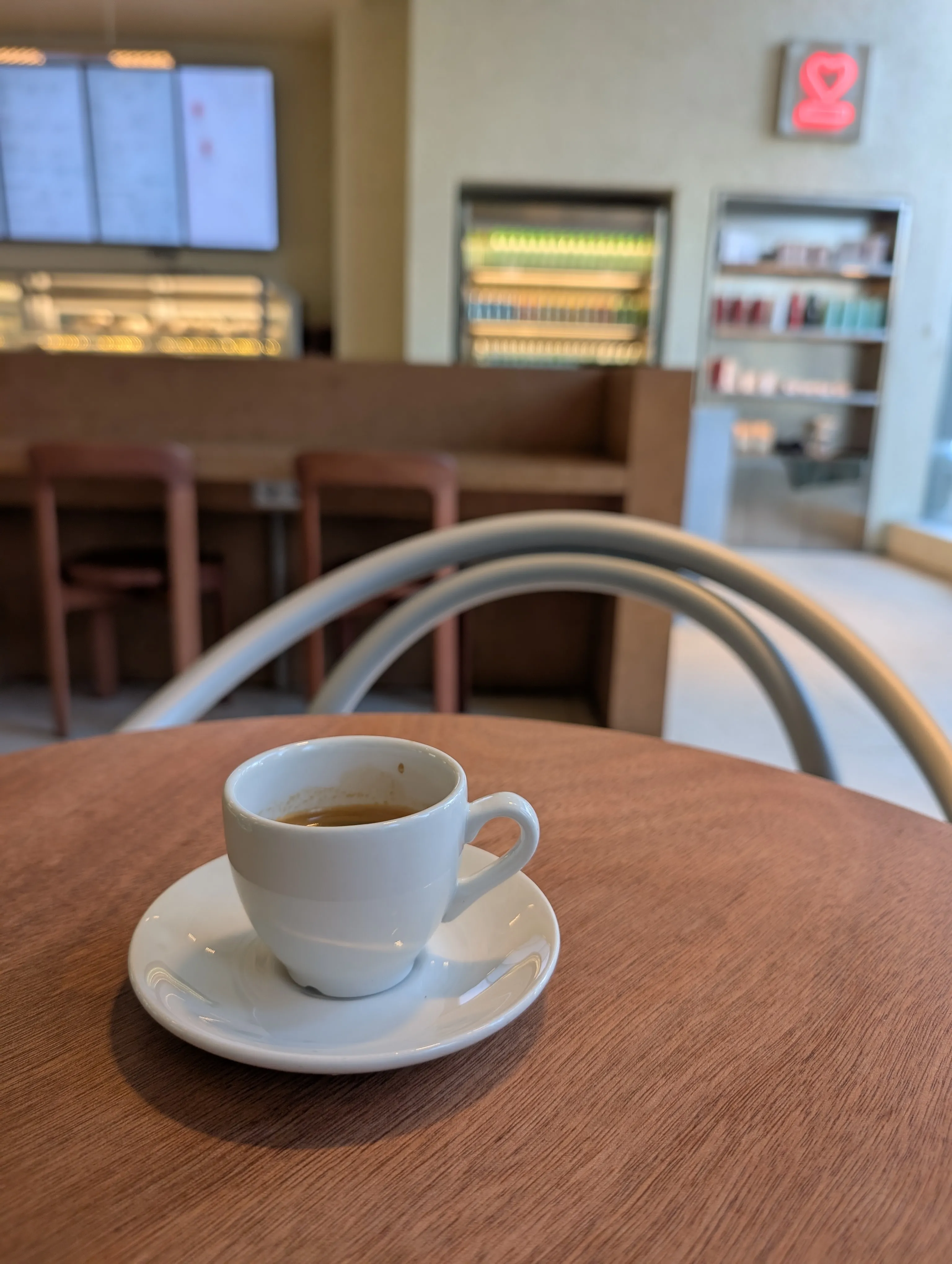 An espresso in a white cup and saucer on a wooden table at Espressolab, with the counter and the menu screens behind it