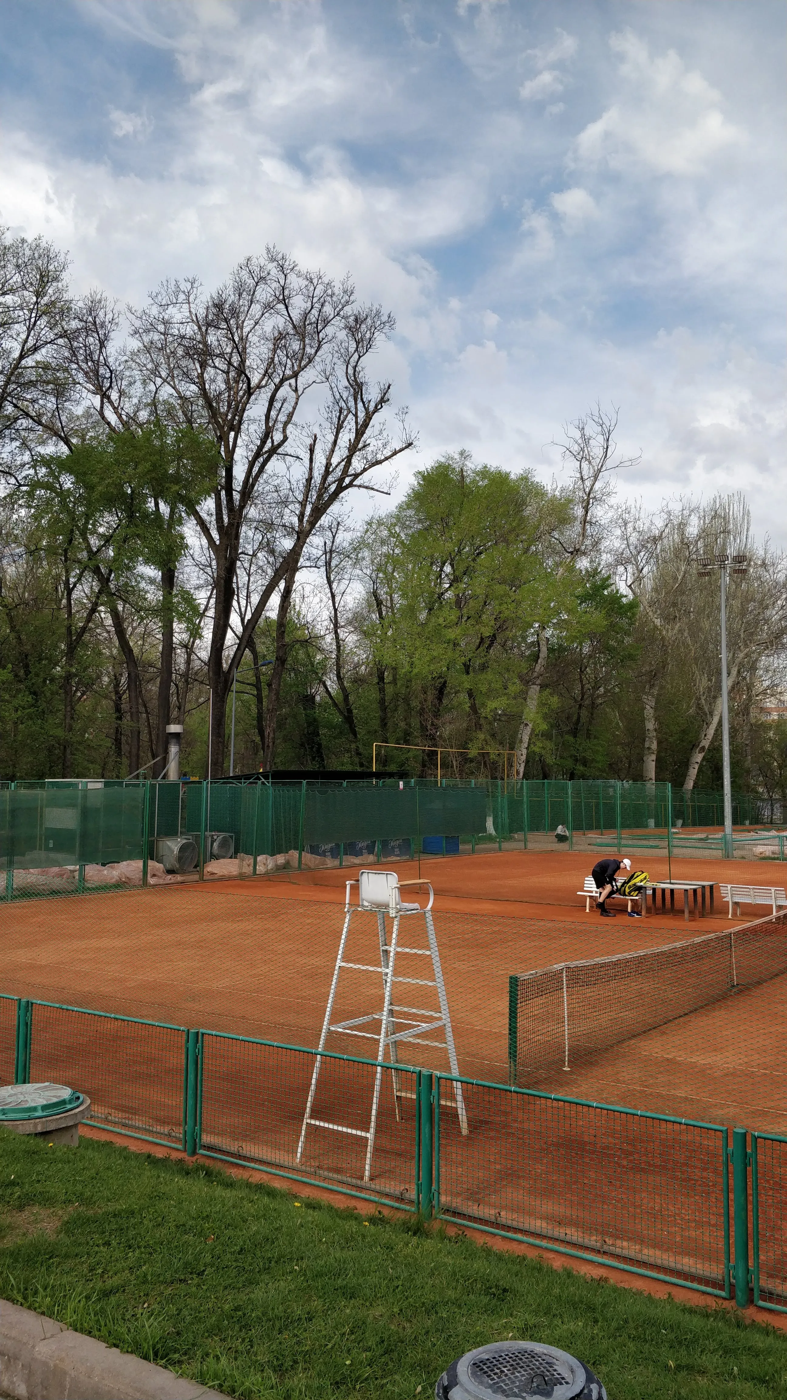 Clay tennis courts among tall bare trees in Gorky Park, their green net fencing run in long lines, a court sweeper at work on the far side