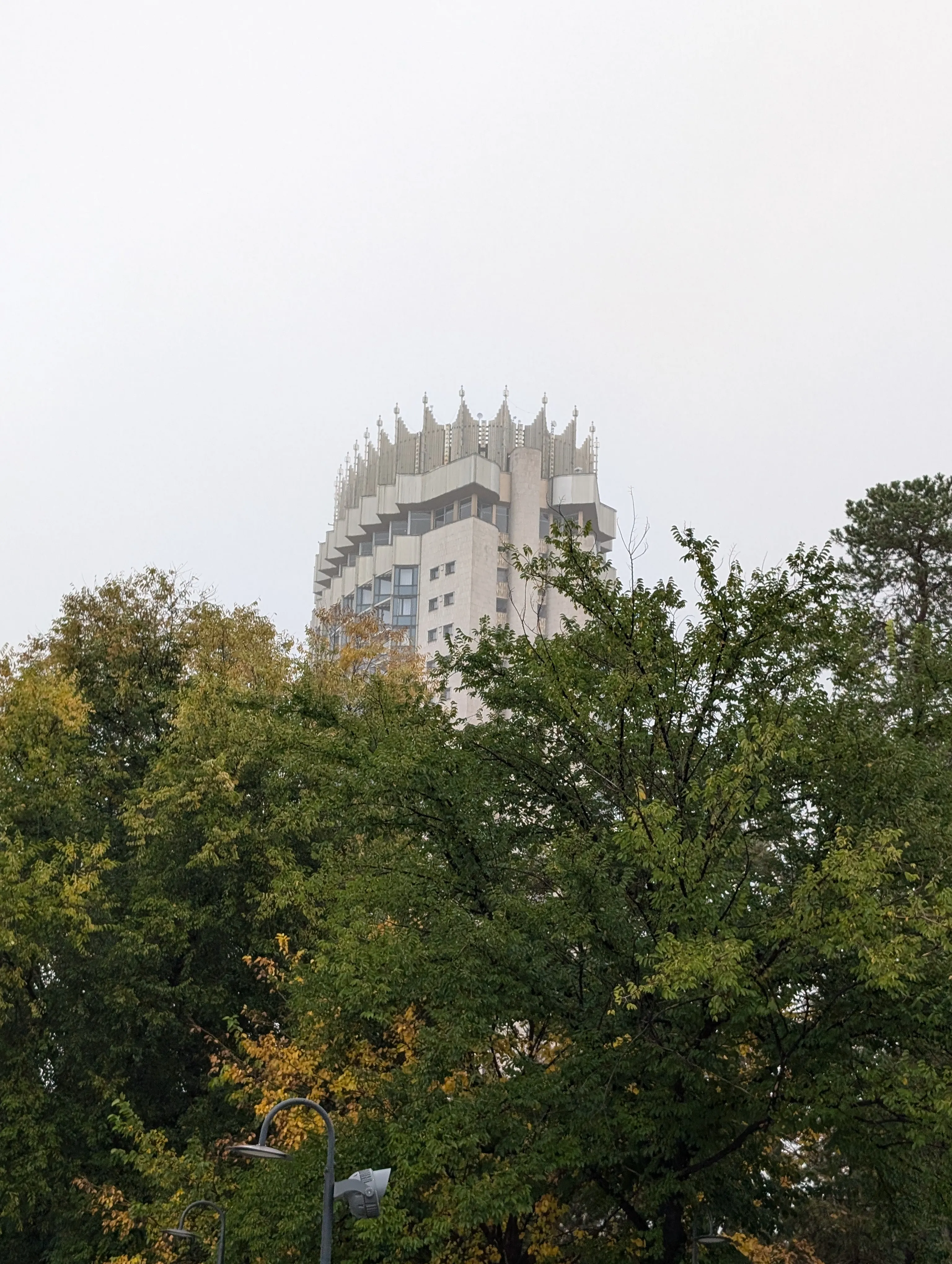 The same tower on an overcast morning, its full crown of gilded fins standing above the treetops against a flat grey sky