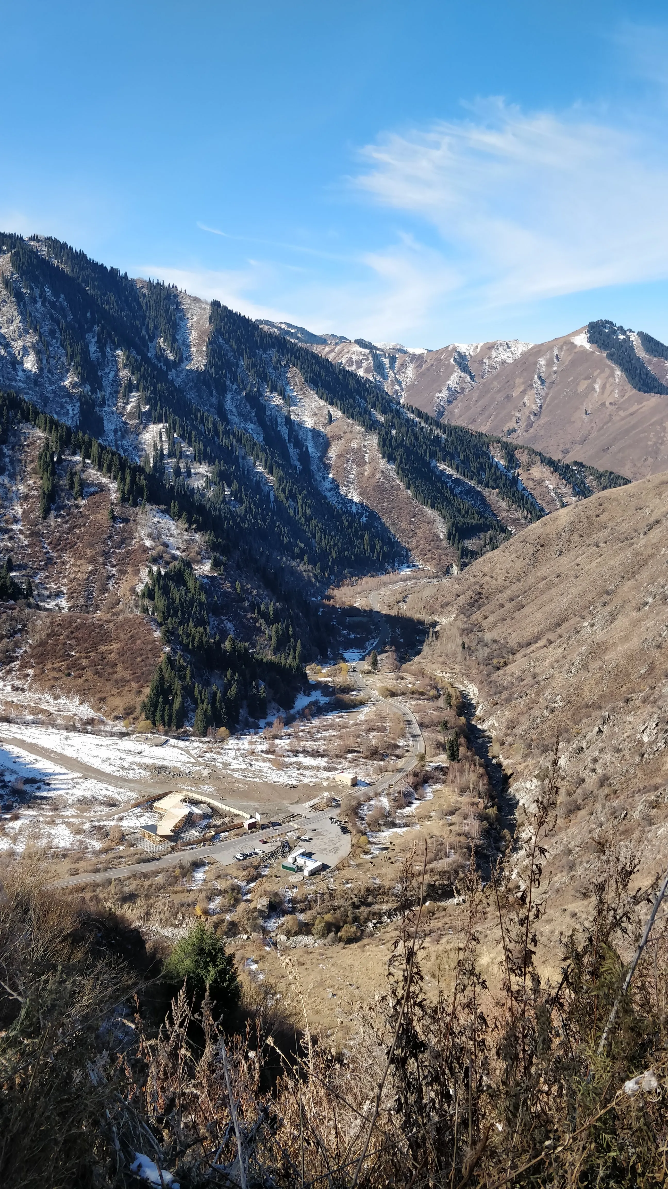 Looking down from the Japanese trail onto the valley floor: the visitor centre and car park beside the road, the river beyond it, and spruce climbing the shaded slope opposite under first snow