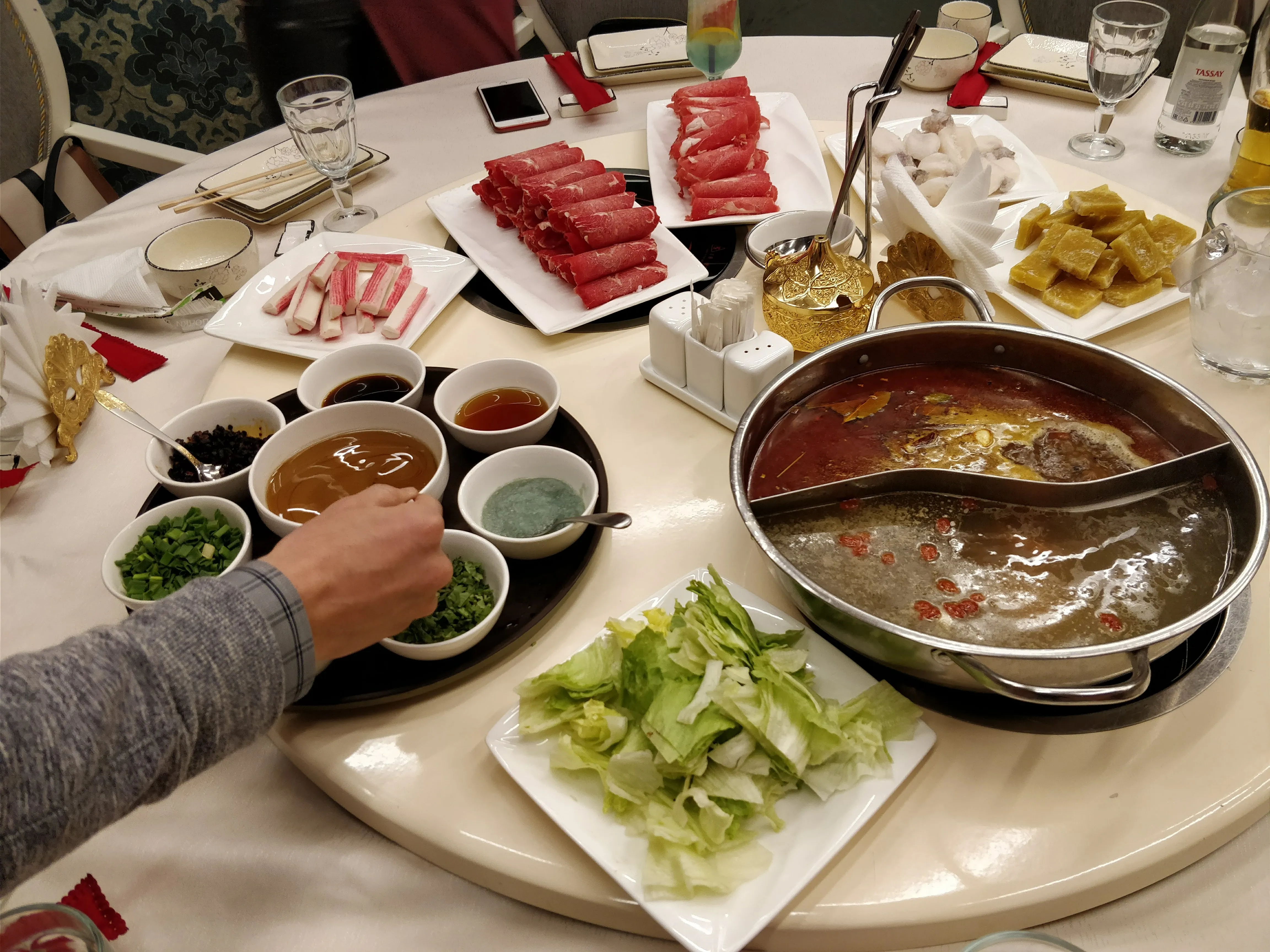 A hot pot at J.Z. Peking Duck: a divided pan of clear and chilli broth in the middle of the table, with plates of rolled raw beef, lettuce and small bowls of sesame and herb sauces around it