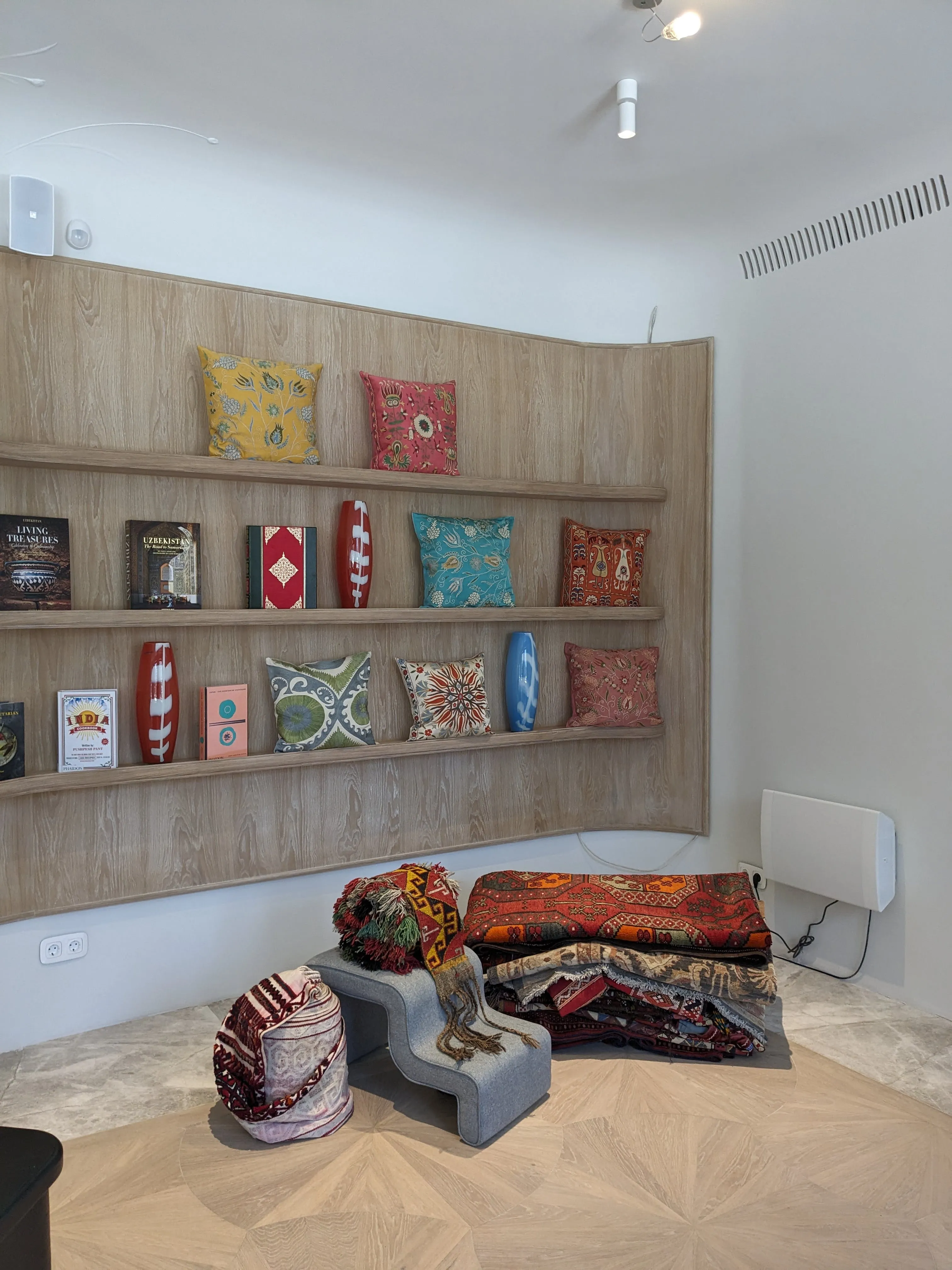 Inside Korkem: a shelf of embroidered cushions in Kazakh ornament above folded textiles and carpets, with a small metal sculpture on a plinth