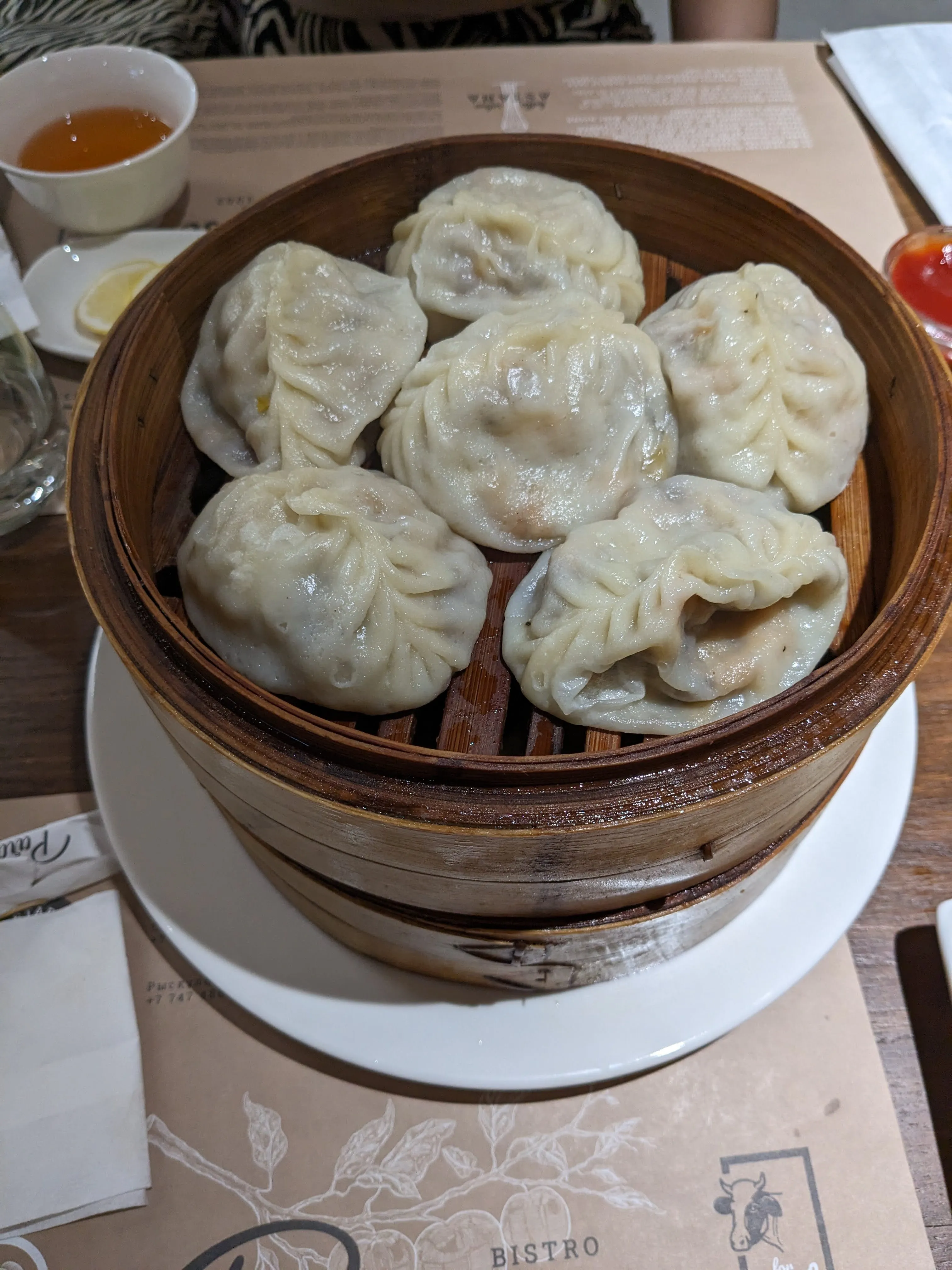 A bamboo steamer of manty at Paradise: six large pleated dumplings, with tea and chilli sauce on the table beside them