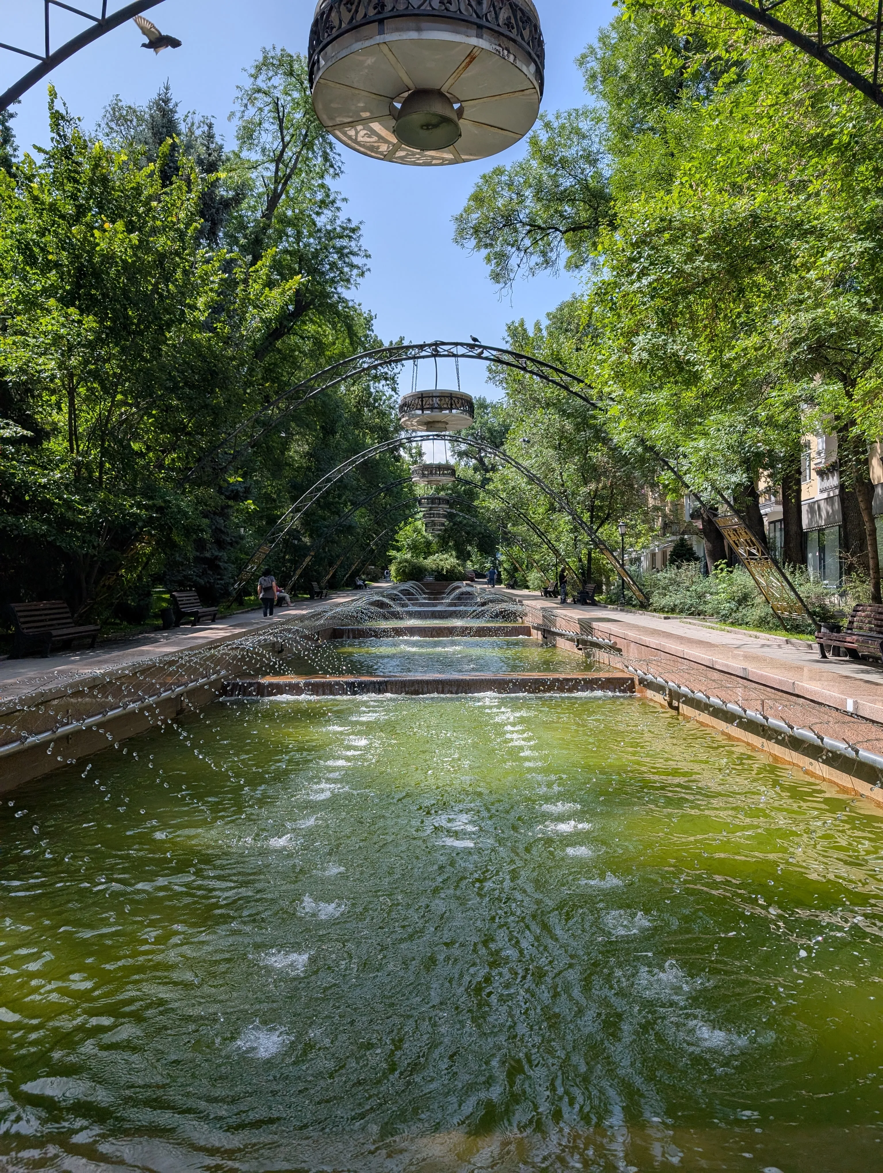 The stepped cascade of the Nedelka fountain under iron arches and trees
