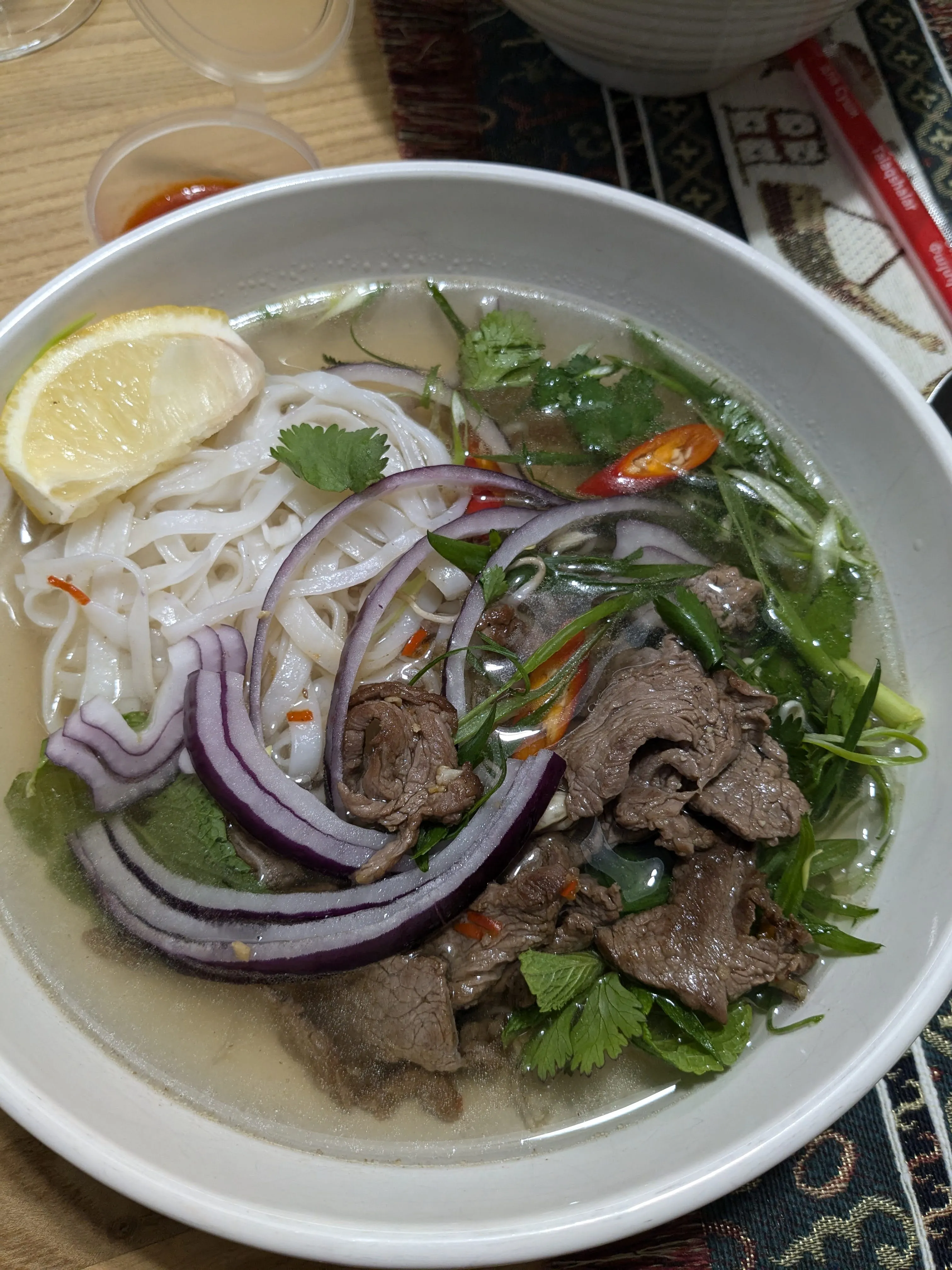 A white bowl of pho bo at Coffeeon SaiGon: flat rice noodles in clear broth under sliced beef, rings of red onion, coriander, spring onion and a wedge of lemon