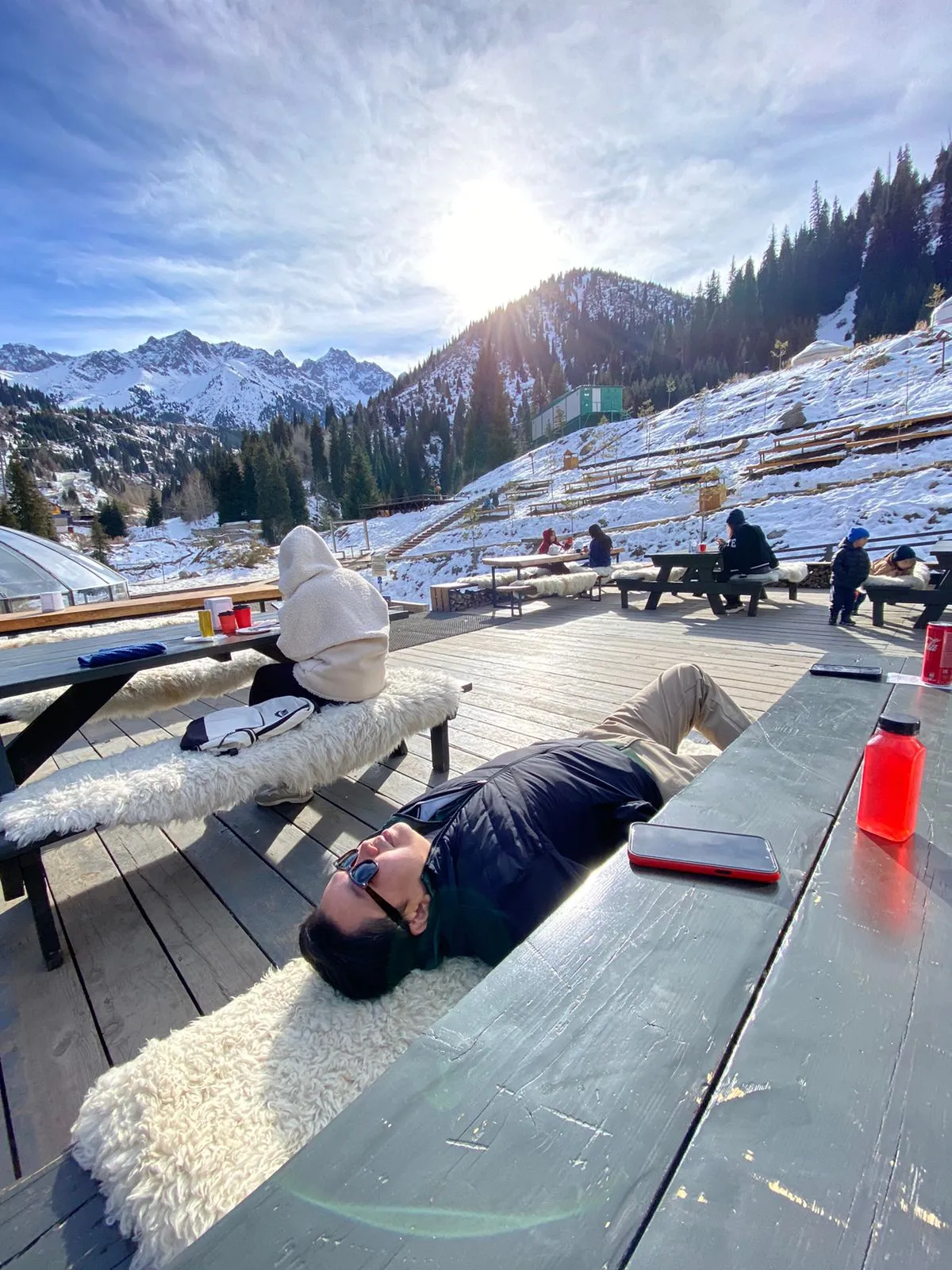 The terrace at Apa Katya in winter: sheepskins over the benches, snow on the slope behind, and the ridge white against the sun