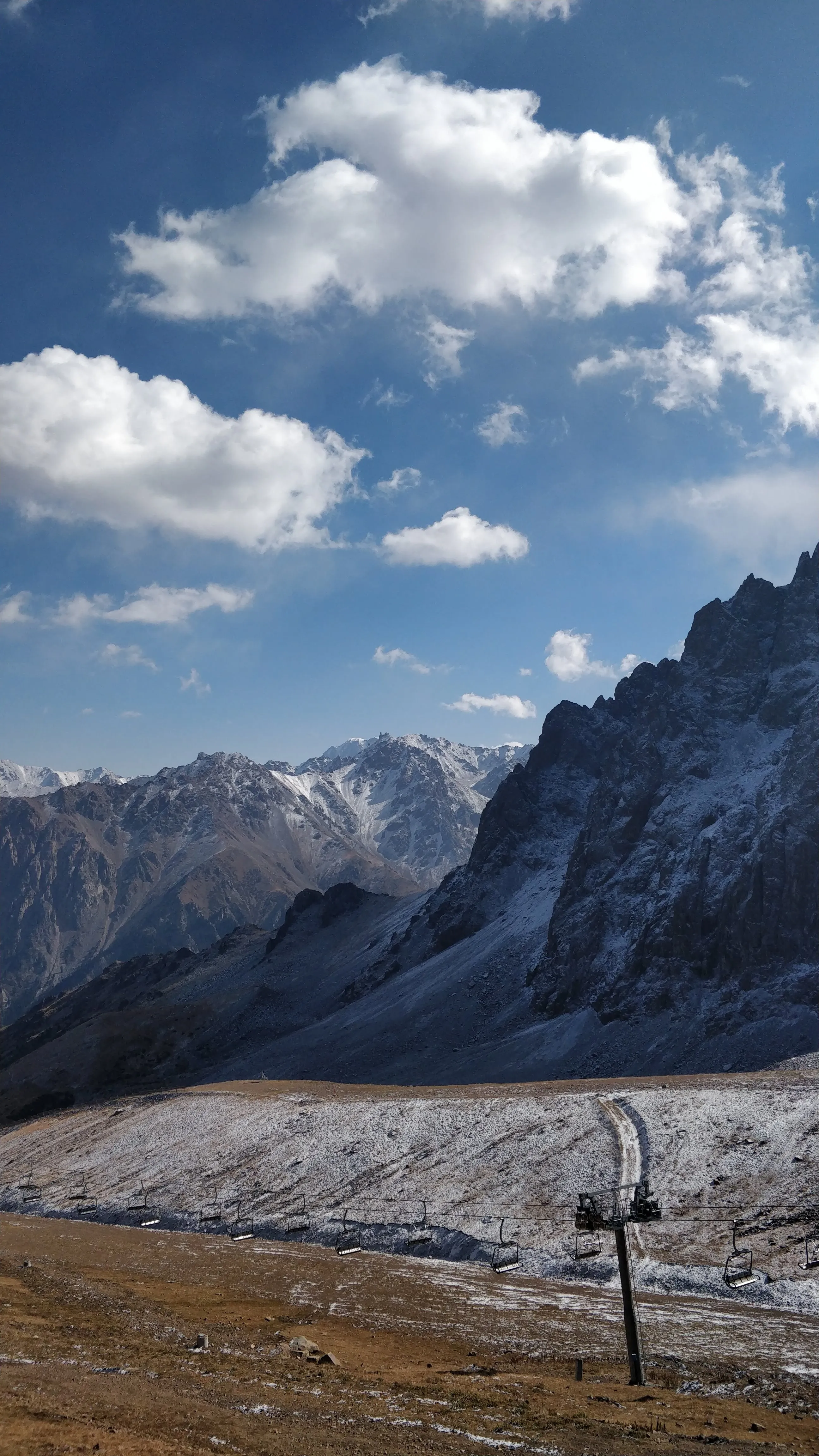 At 3,200 metres above Shymbulak: an empty chairlift line crossing a slope under fresh snow, with a rock ridge above