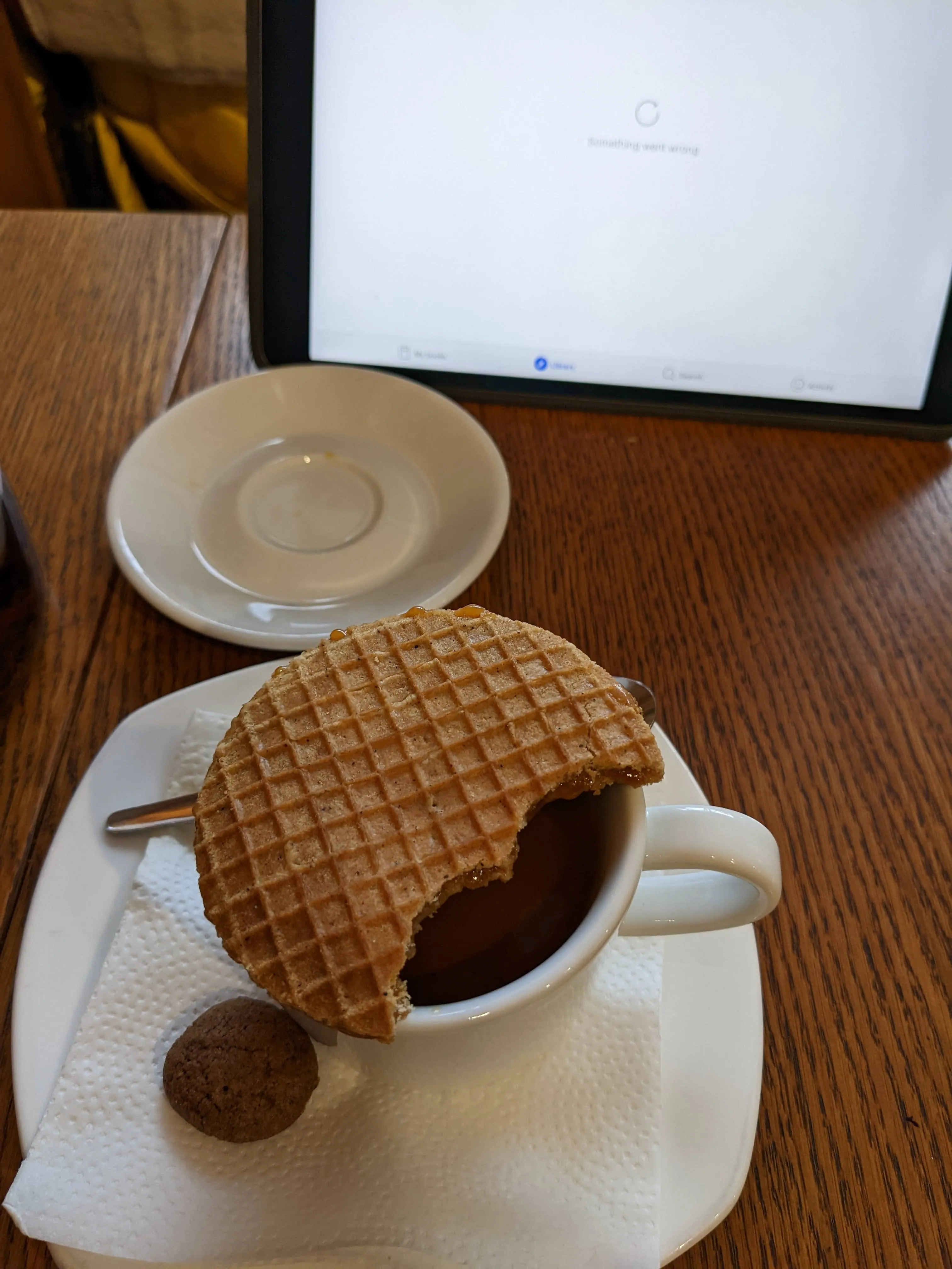 A stroopwafel resting on the rim of an espresso cup at Bowler, softening over the steam, with a small chocolate biscuit beside it