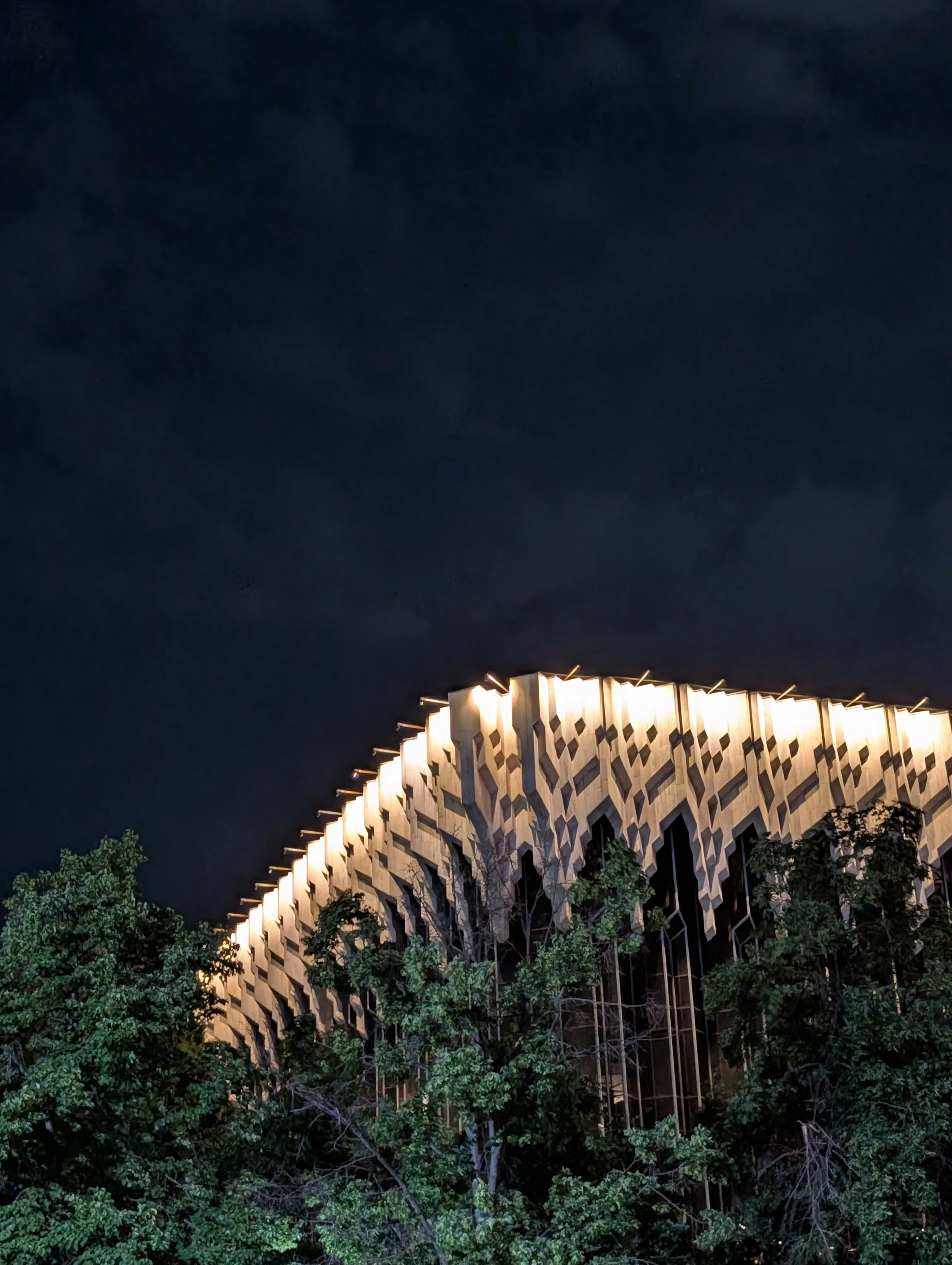 The curved relief wall of the Telecentre lit from below after dark