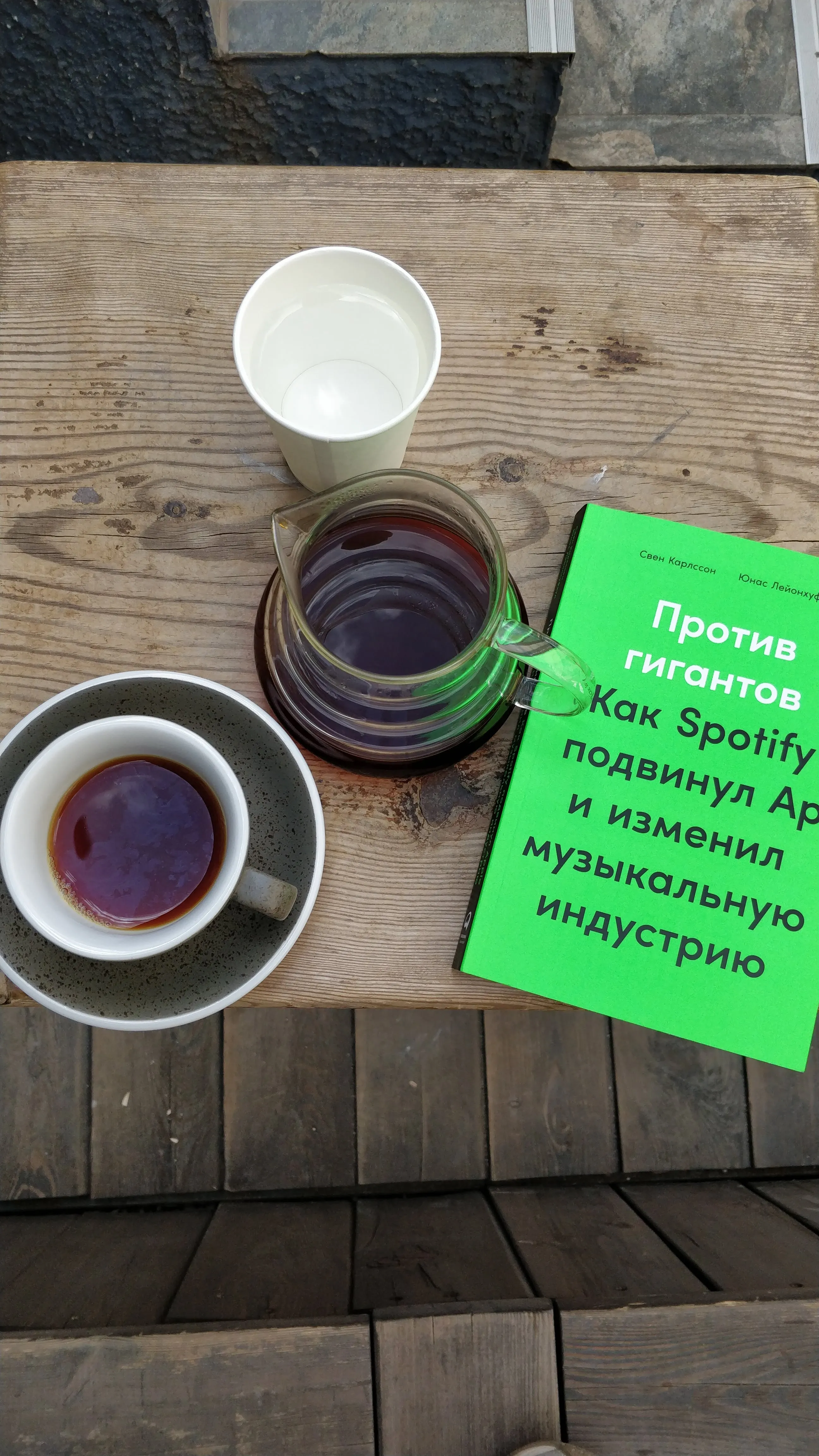 A pour-over carafe and a cup of black coffee on the terrace at Probarista, a paperback laid face down beside them
